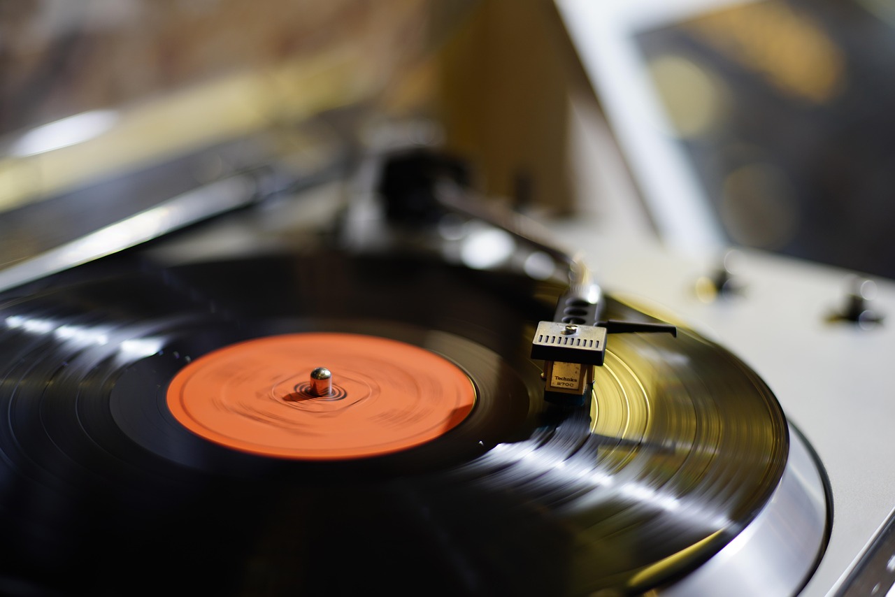 Mână care trage un disc de vinil dintr-un raft plin, lângă o fereastră cu lumină de primăvară